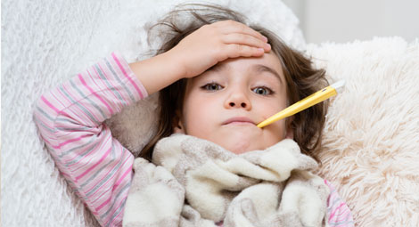 Ill child with a thermometer in her mouth. She is holding her forehead.
